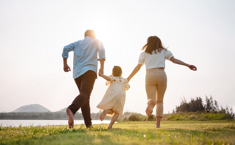 Happy family with while life insurance running in a meadow at sunset